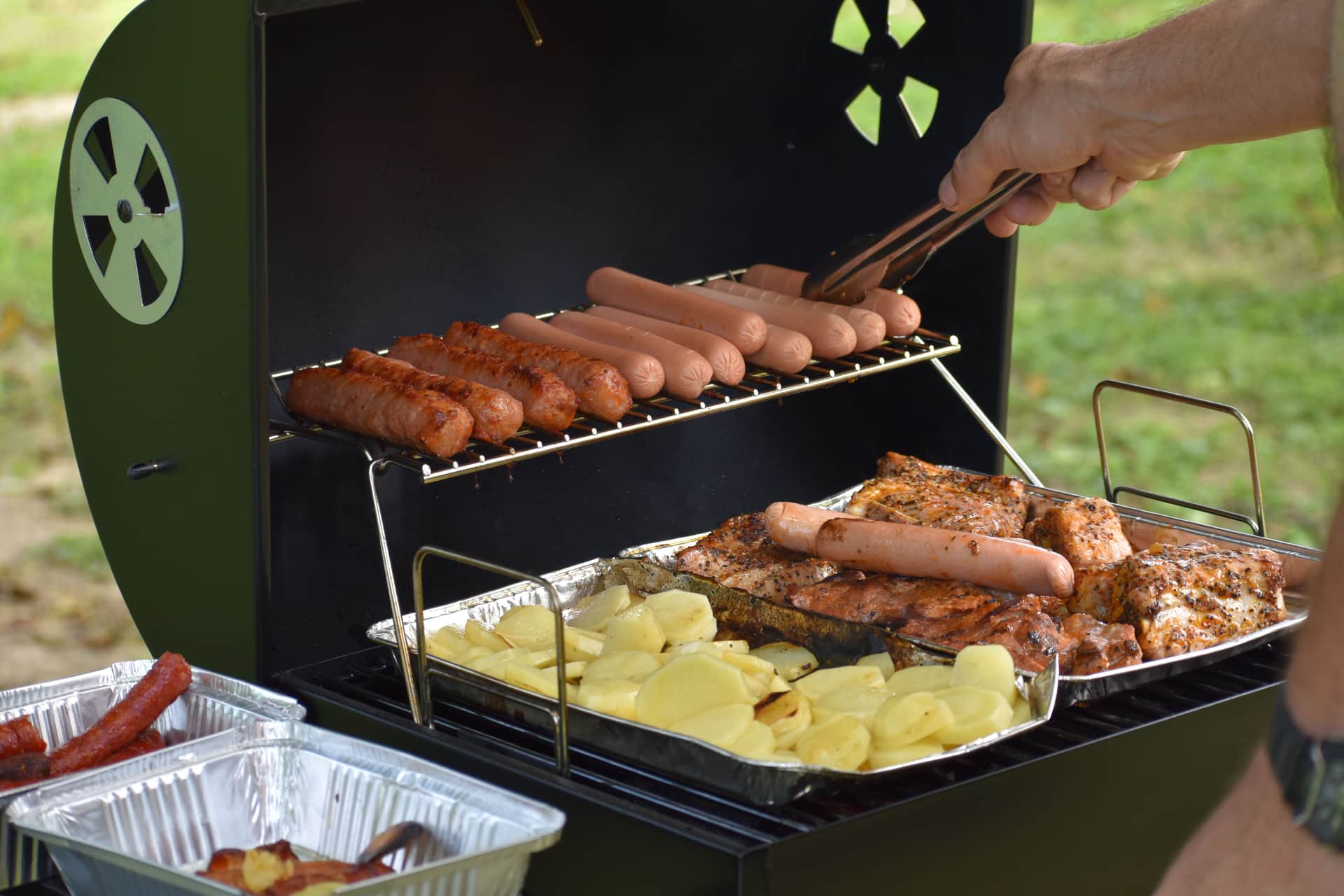 A charcoal barbecue smoker with thin smoke rising outdoors